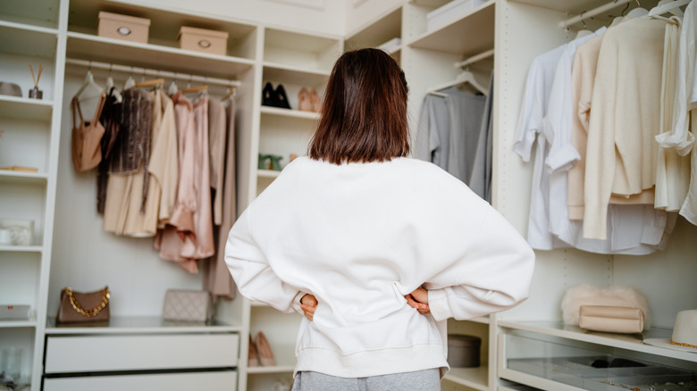 Một người phụ nữ có mái tóc màu nâu vàng đứng trong tủ quần áo không cửa ngăn để tìm đồ.