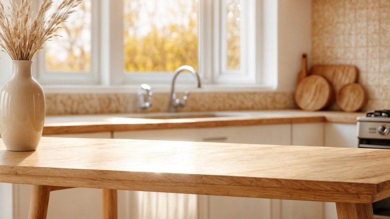 Bàn gỗ trong nhà bếp với tủ màu trắng, tấm lót gạch và cửa sổ trên bồn rửa