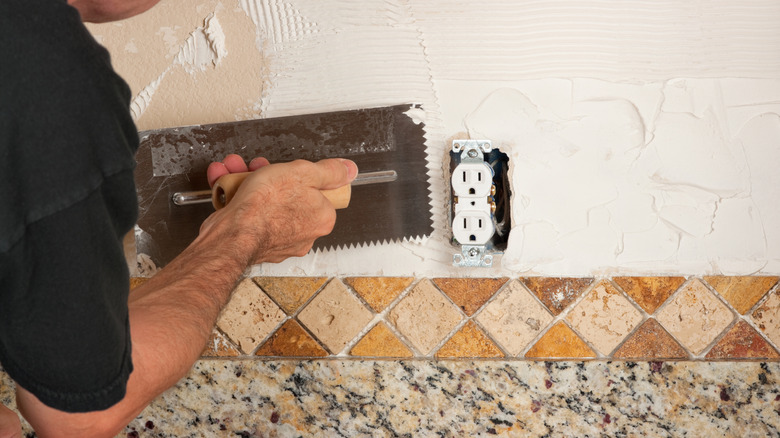 Một người đang áp dụng một phần ngược phong cách đường chéo Tuscan trong các tông màu trái đất vào một bức tường.