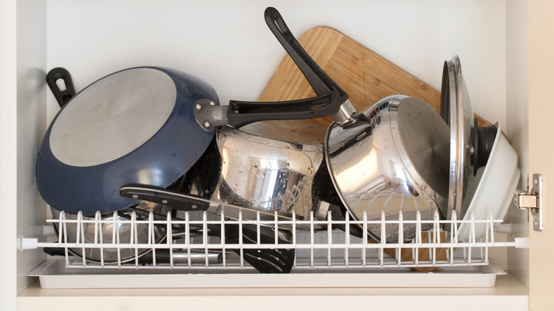 đống nồi, chảo, thớt và nắp đậy lộn xộn trên kệ sấy tủ