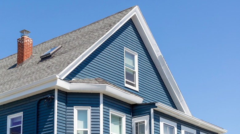 Bên ngoài của một ngôi nhà có mái nhà màu xám, mặt xanh trung bình và trang trí màu trắng