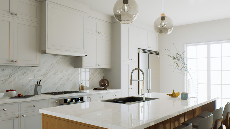 Nhà bếp màu trắng với quầy đá cẩm thạch và mặt sau, thiết bị bạc và đảo với chỗ ngồi