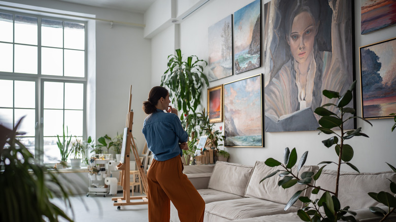 Người phụ nữ nhìn vào bức tường phòng trưng bày hiện đại trong phòng khách với nghệ thuật và thực vật lớn