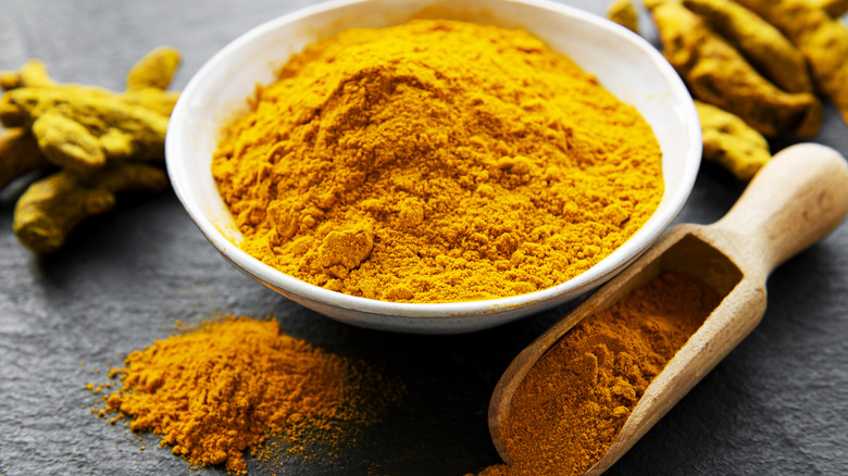 Bột nghệ trong bát, muỗng và rễ trong nền