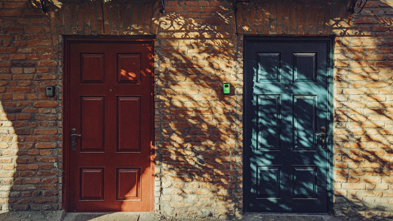 Cửa màu đỏ và ngọc lục bảo/màu xanh da trời trên tòa nhà gạch với bóng của cây