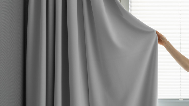 Người phụ nữ giữ một bên của bảng treo màu xám rắn được treo bên cạnh cửa sổ