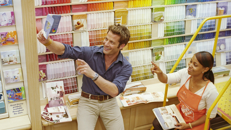 Nate Berkus giữ một mẫu sơn trước một bức tường màu sắc màu trong một lối đi của Home Depot