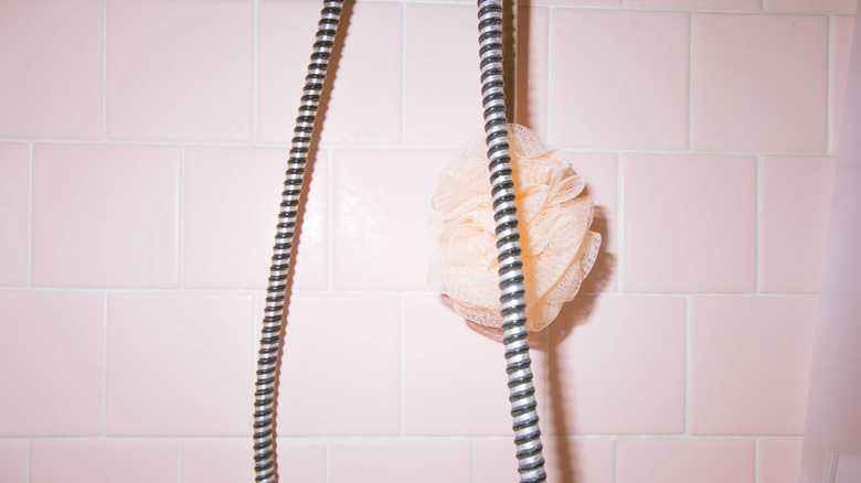 Ngói màu hồng nhạt với một loofah màu hồng và dây của một vòi hoa sen cầm tay