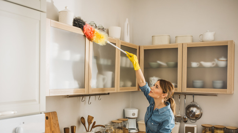 Người phụ nữ mặc áo jean phủ bụi trên cùng của một cái tủ trong một nhà bếp màu be