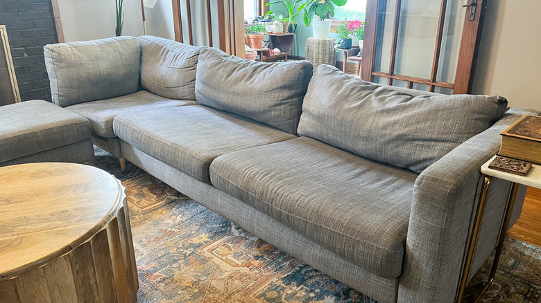 Ghế sofa màu xám chảy xệ trong phòng khách với đệm chảy xệ, mòn