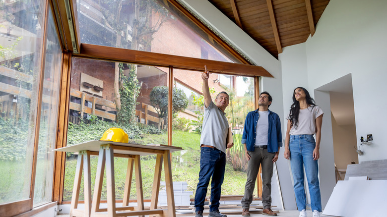 Nhà thầu làm việc tại một ngôi nhà, nói chuyện với nam và nữ trong khi chỉ vào trần nhà