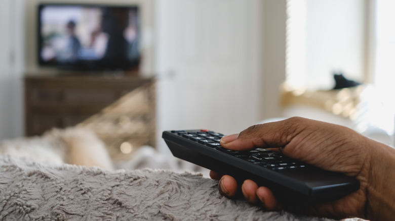 Bàn tay của người trên giường giữ từ xa với TV trong nền