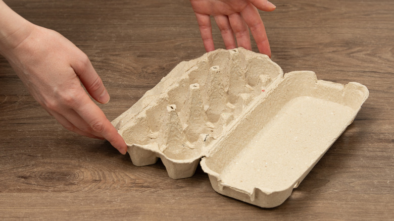 người cầm thùng trứng rỗng trên bề mặt gỗ