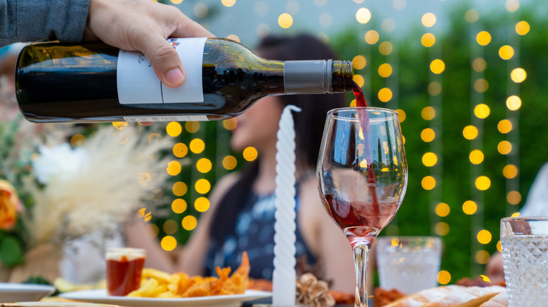 Người đàn ông rót một ly rượu vang đỏ từ chai khi đang ở bữa tiệc tối ngoài trời