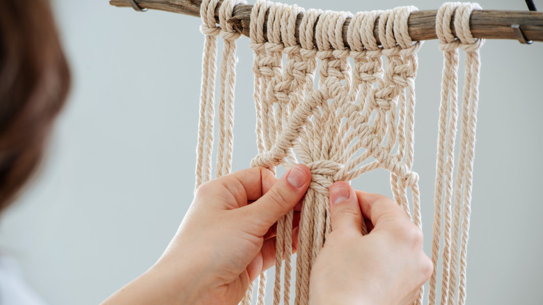 Người phụ nữ buộc macrame trên một cây gậy.