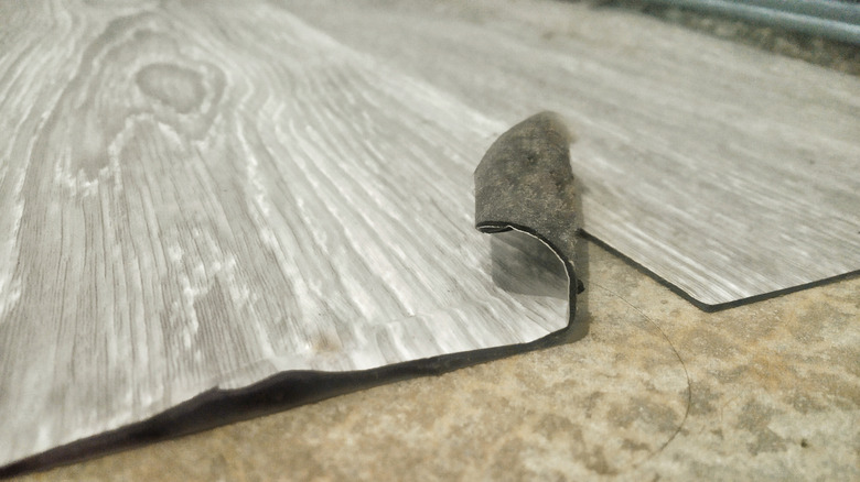 Một tấm vinyl in vân gỗ màu xám uốn cong ở một cạnh