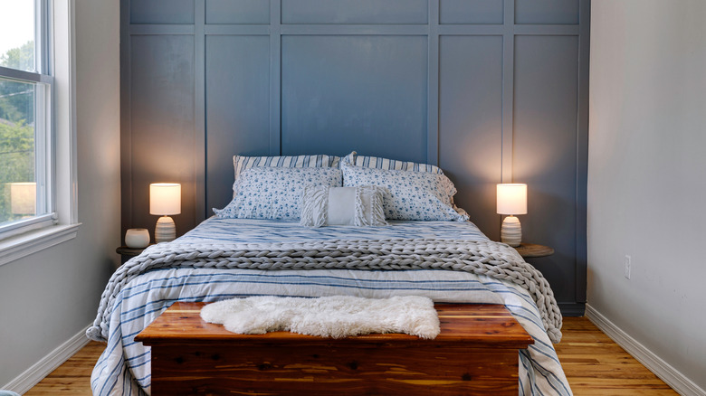 Một phòng ngủ nhỏ với sàn gỗ, tủ gỗ, bàn phụ, giường với ga trải giường màu xanh lam và bức tường tạo điểm nhấn màu xanh lam với ván và ván sàn