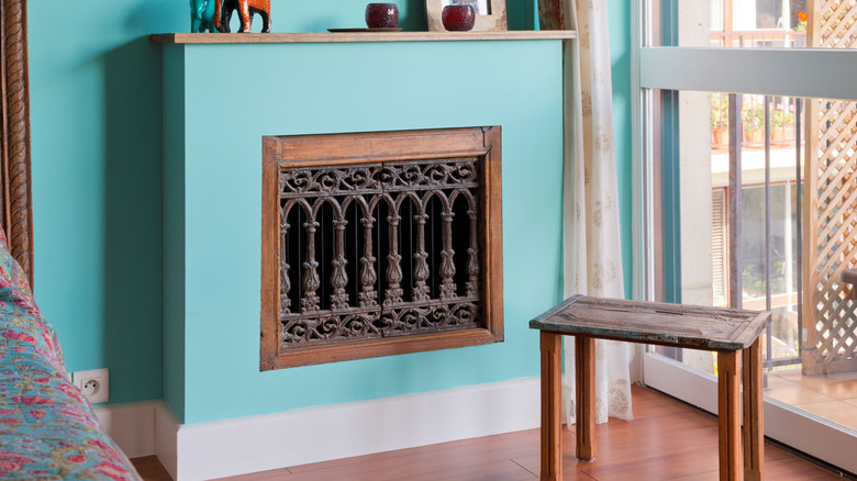 Một lỗ mở tối màu được trang trí công phu trên nắp bộ tản nhiệt màu xanh nhạt đặt trên bức tường màu xanh lam