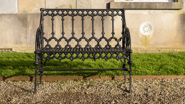 Chiếc ghế băng hai chỗ ngồi bằng gang với thiết kế phức tạp nằm trên con đường rải sỏi trong vườn.