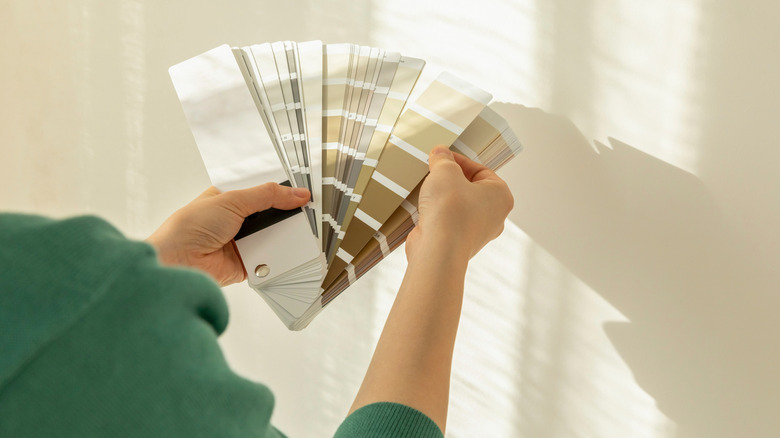 Bàn tay nhìn qua bảng màu sơn trung tính treo trên bức tường màu be.
