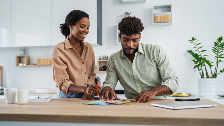 Người phụ nữ và người đàn ông đang xem các mẫu màu trên mặt bàn bếp