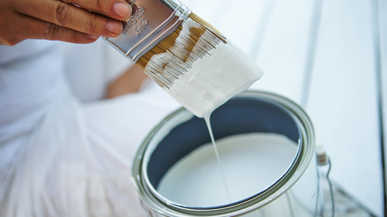 Một người nhúng cọ sơn vào thùng sơn