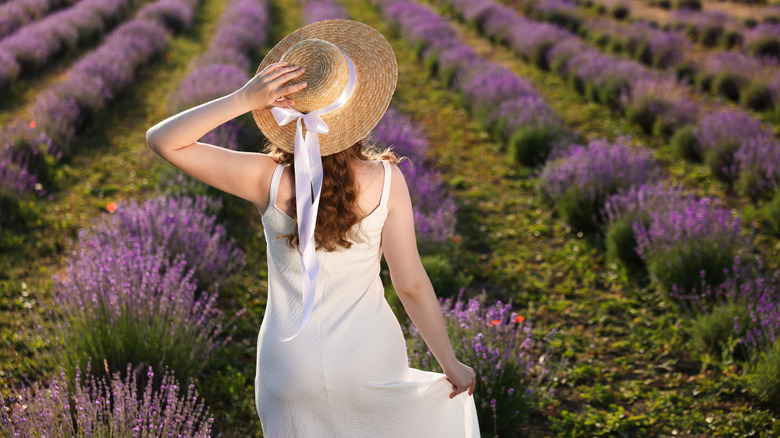 Người phụ nữ đội mũ xuân và mặc váy đứng trên cánh đồng hoa