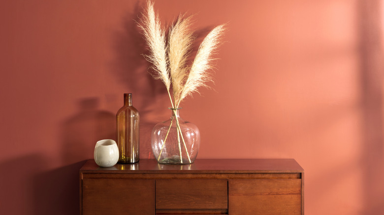 Lọ thủy tinh trang trí đặt trên bàn gỗ trước bức tường sơn màu đất nung