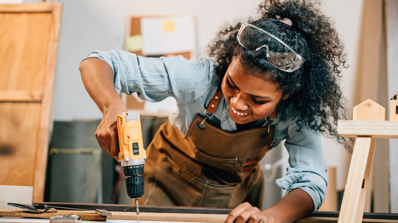 Một người phụ nữ mỉm cười khi khoan vào tấm ván gỗ