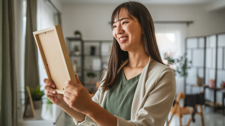 người phụ nữ mỉm cười cầm khung ảnh