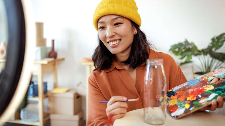 Một người đội mũ màu vàng vẽ một chai thủy tinh rỗng bằng bảng màu đầy màu sắc.