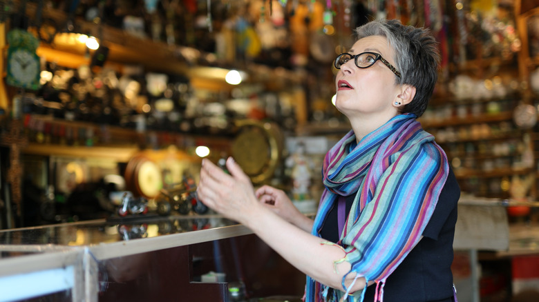 Một người phụ nữ lớn tuổi nhìn thấy thứ gì đó ở cửa hàng đồ cổ đầy màu sắc