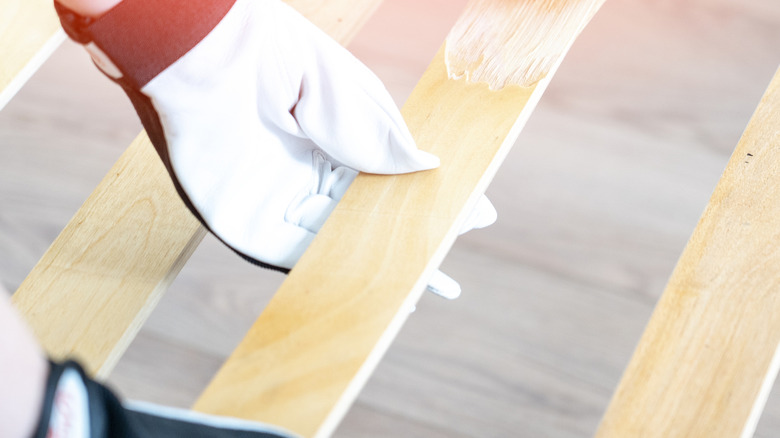 Một bàn tay đeo găng giữ chặt thanh gỗ được sơn một phần