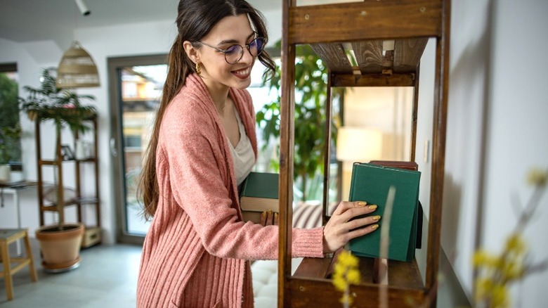 Người phụ nữ xinh đẹp sắp xếp sách trên kệ ở nhà