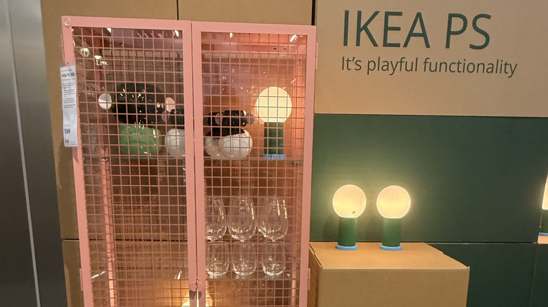 Tủ quần áo giống tủ kính màu hồng tại IKEA được bao quanh bởi đèn, hộp và bát đĩa