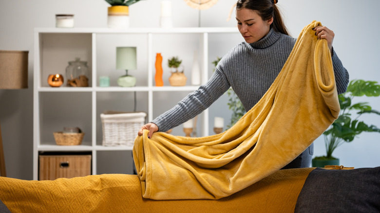 Người phụ nữ gấp chiếc chăn ném màu vàng vàng