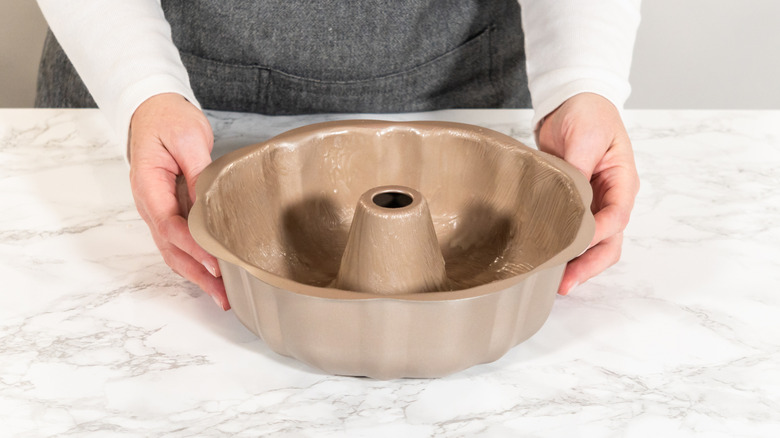 Bàn tay phụ nữ quanh chiếc chảo Bundt đặt trên quầy đá cẩm thạch