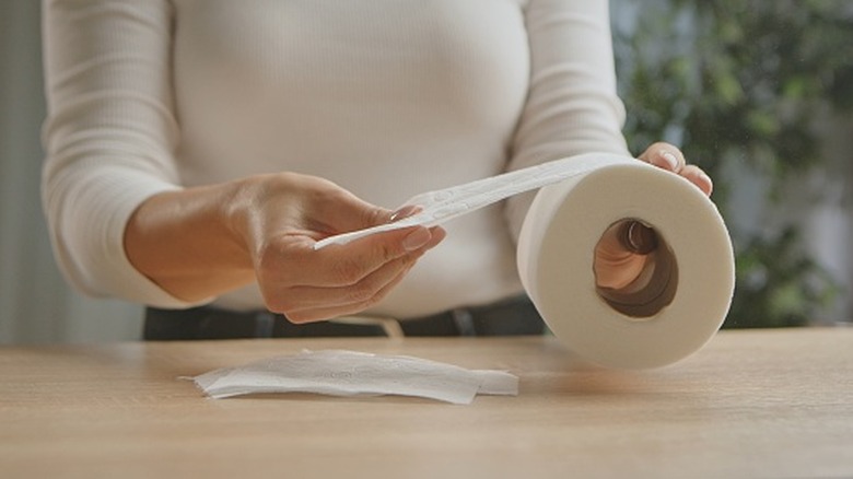 Một người phụ nữ ngồi ở bàn trong khi cầm một cuộn giấy vệ sinh