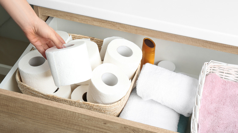 người lấy cuộn giấy vệ sinh từ ngăn kéo trong phòng tắm