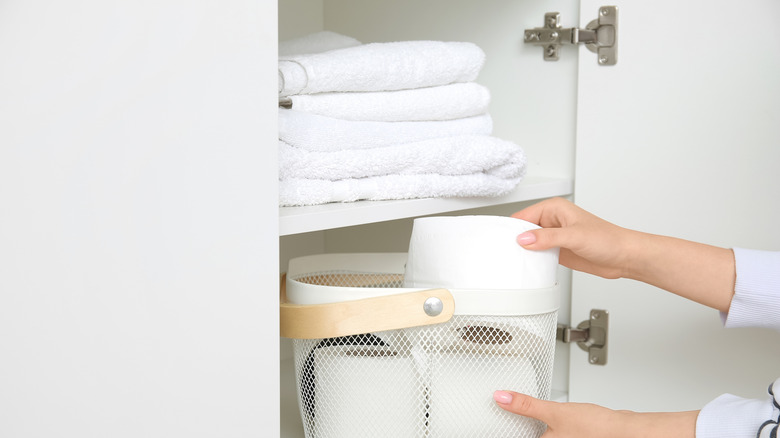 Người lấy cuộn giấy vệ sinh ra khỏi giỏ kim loại trong tủ quần áo