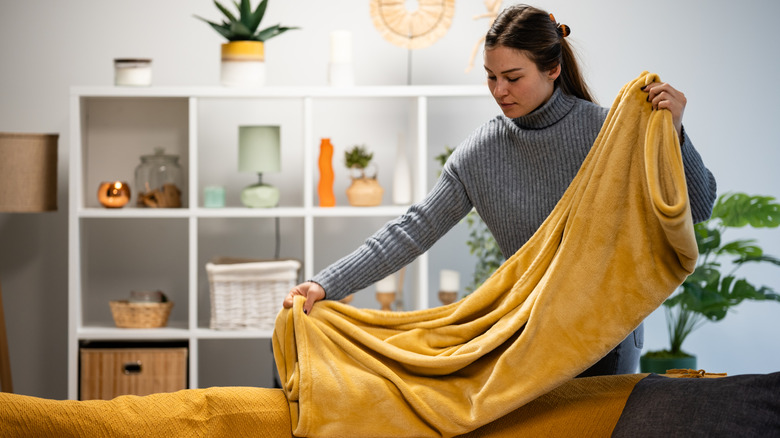 Người phụ nữ gấp chiếc chăn màu vàng trong phòng khách