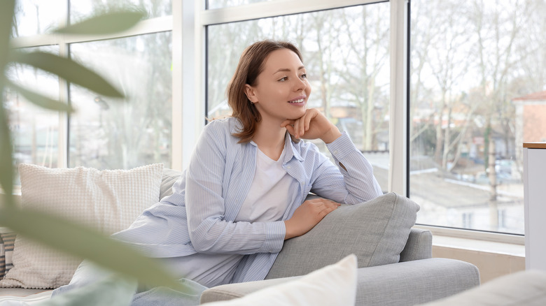 Một người ngồi trên chiếc ghế dài màu xám nhìn ra cửa sổ với một cái cây ở phía trước