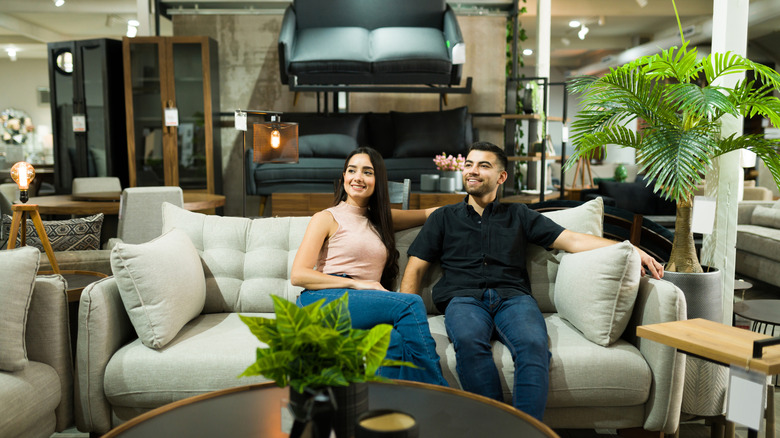 Hai người ngồi trên ghế sofa trong một cửa hàng nội thất có đầy đủ các món đồ phòng khách hiện đại.