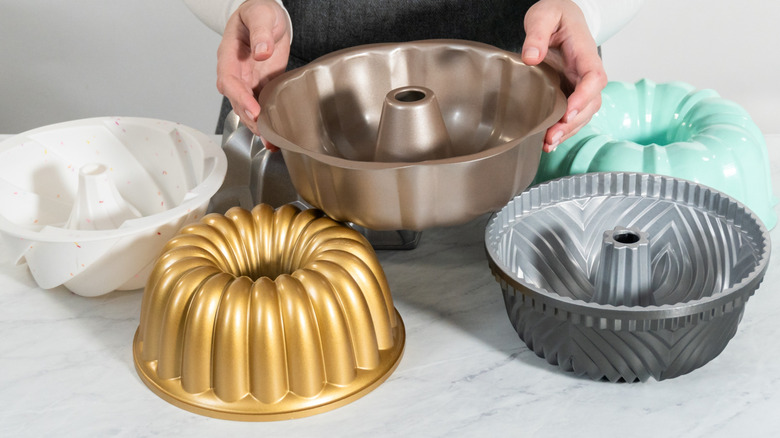 Tay cầm một chiếc chảo Bundt với các màu/kiểu chảo khác nằm rải rác xung quanh