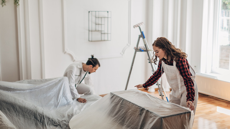 Một cặp vợ chồng đang bọc đồ đạc bằng nhựa trước khi sơn phòng