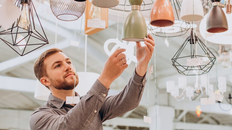 Người đàn ông đang xem xét các lựa chọn chiếu sáng trên cao trong một cửa hàng tiết kiệm